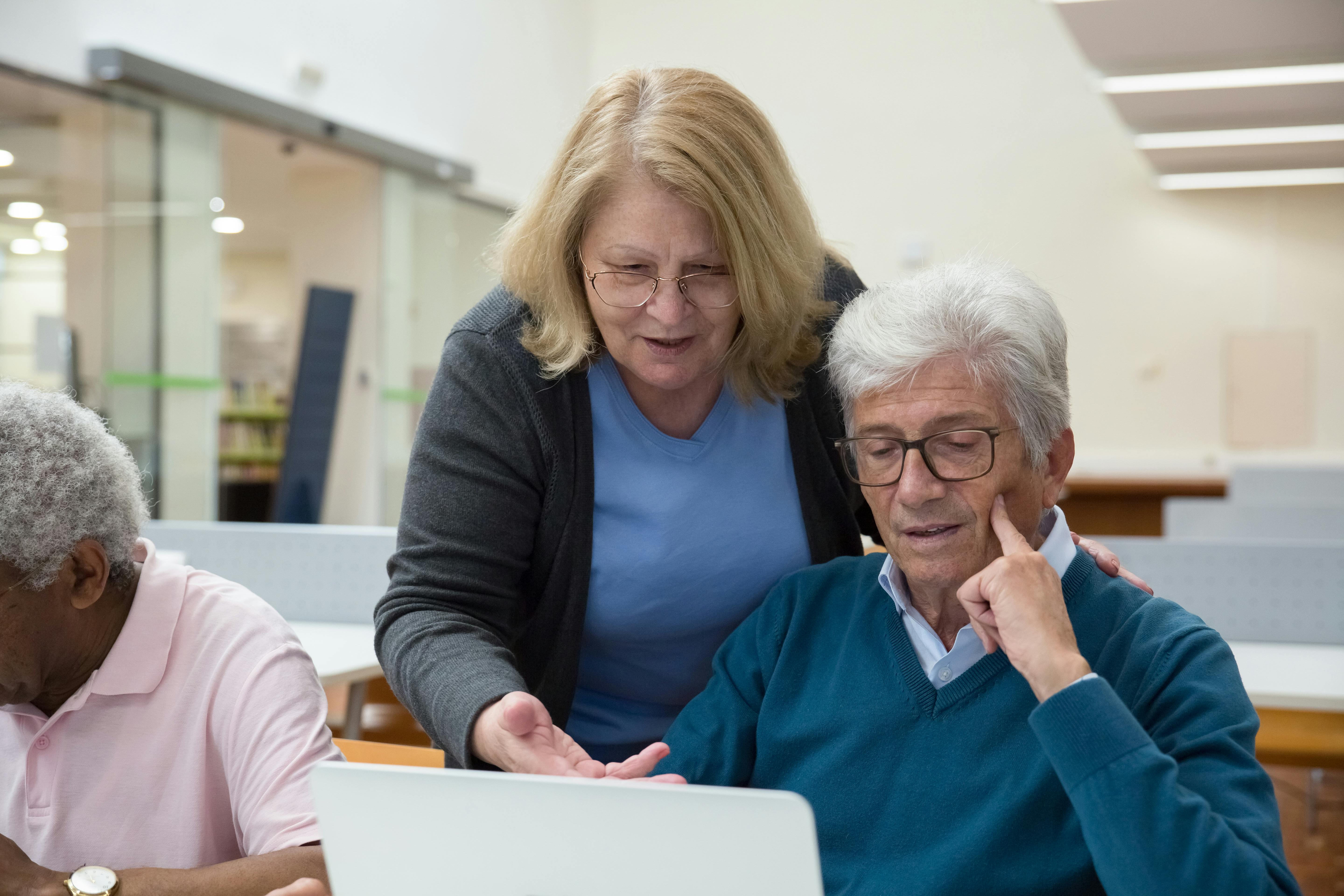 Woman teaching man to use a laptop